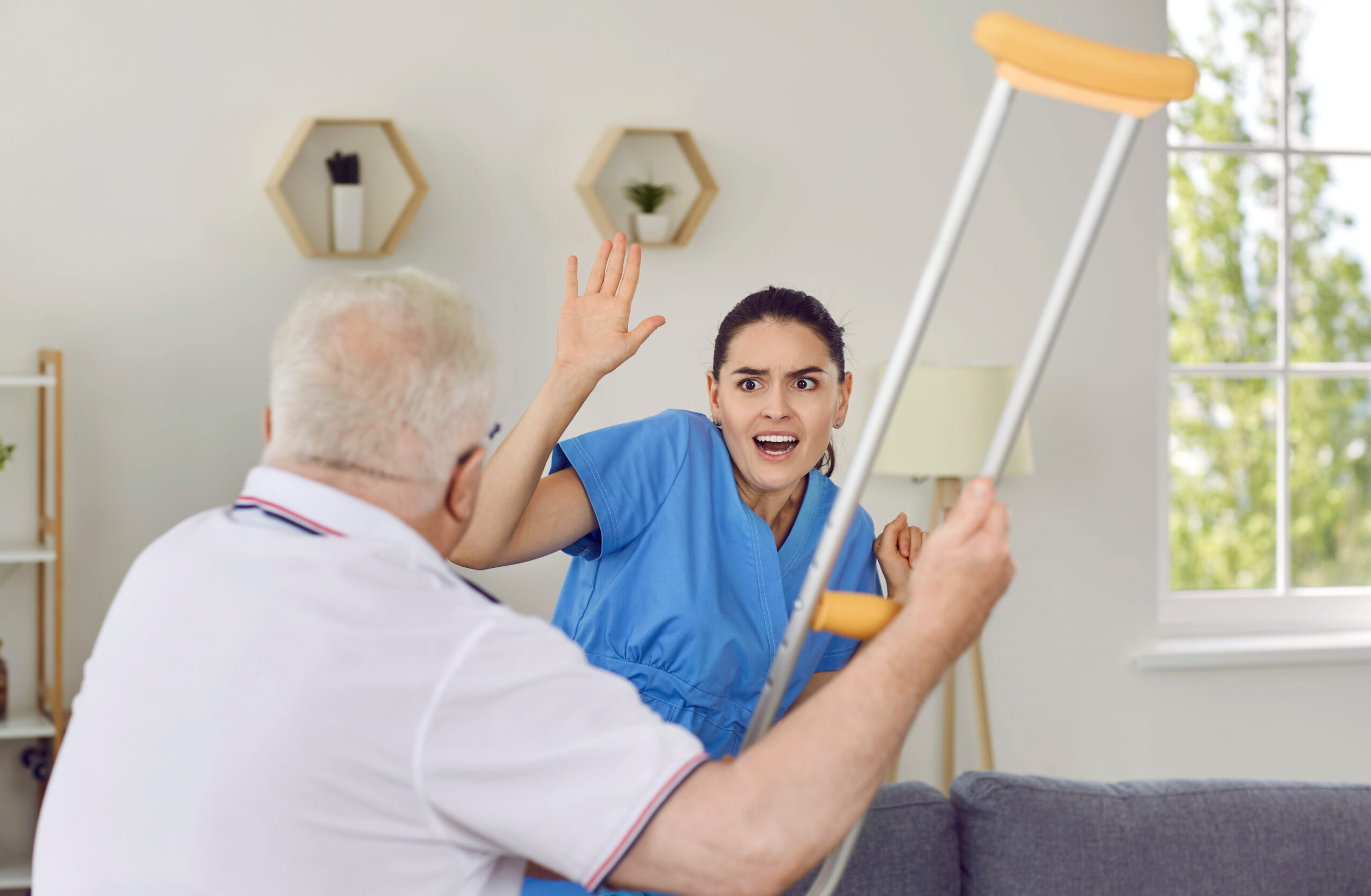 Angry elderly man threatening nurse to hit her with crutch